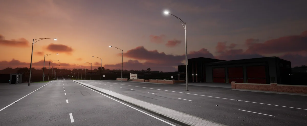 An empty small-town road at sunset, streetlights lit, passing a fire station with red bay doors