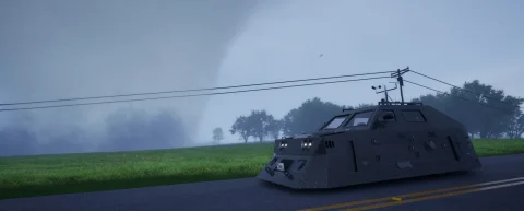 An armoured chaser vehicle parked roadside under power lines, a tornado beyond the treeline
